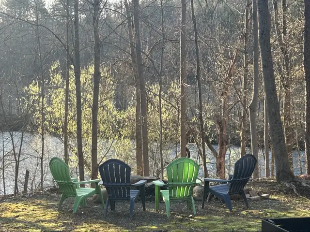 Four Adirondack chairs facing the Battenkill River beneath tall trees