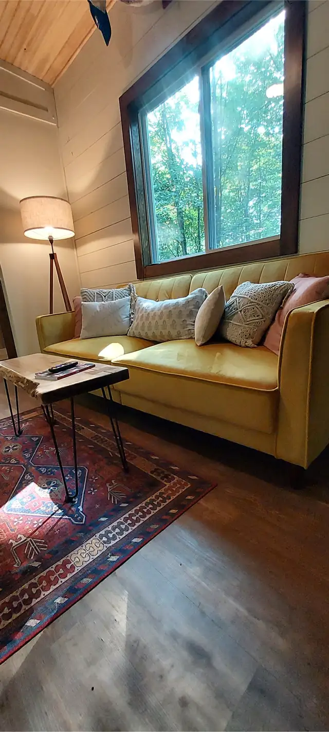 Tiny house living room in daylight: yellow couch under a big window looking onto green trees