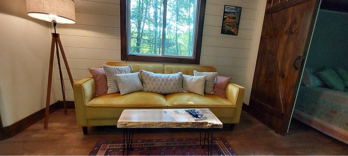 Tiny house living room with a yellow couch and a sliding barn door open to the bedroom