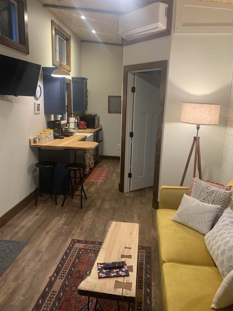 Tiny house kitchen and living area in the evening: navy-blue cabinets, butcher-block counters, yellow couch
