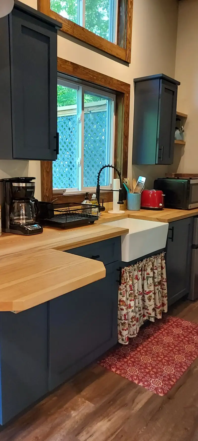 Tiny house kitchen close-up: white farmhouse sink, navy cabinets, red toaster, and coffee maker