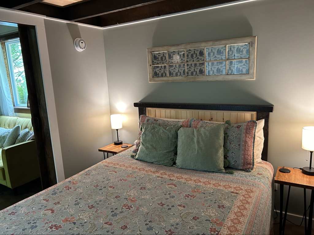Tiny house bedroom: bed with sage-green bedding and pillows, two nightstands with lamps