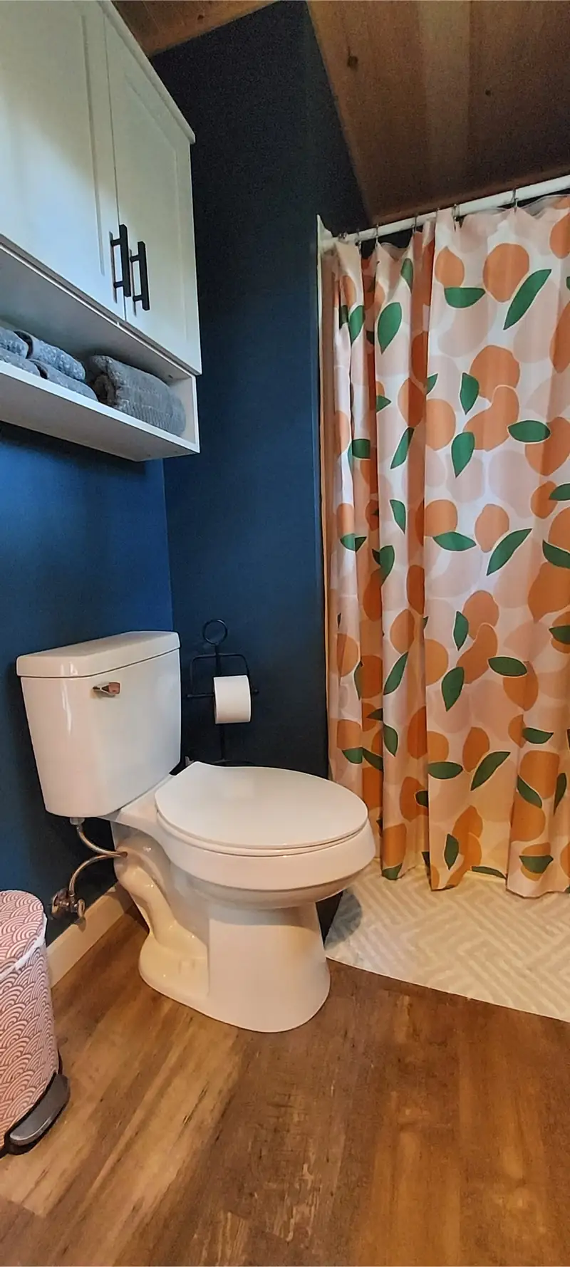Tiny house bathroom: navy walls, white toilet, and a shower curtain with an orange and leaf pattern