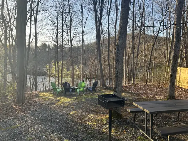 Four Adirondack chairs near the Battenkill River, with a charcoal grill and picnic table in the foreground